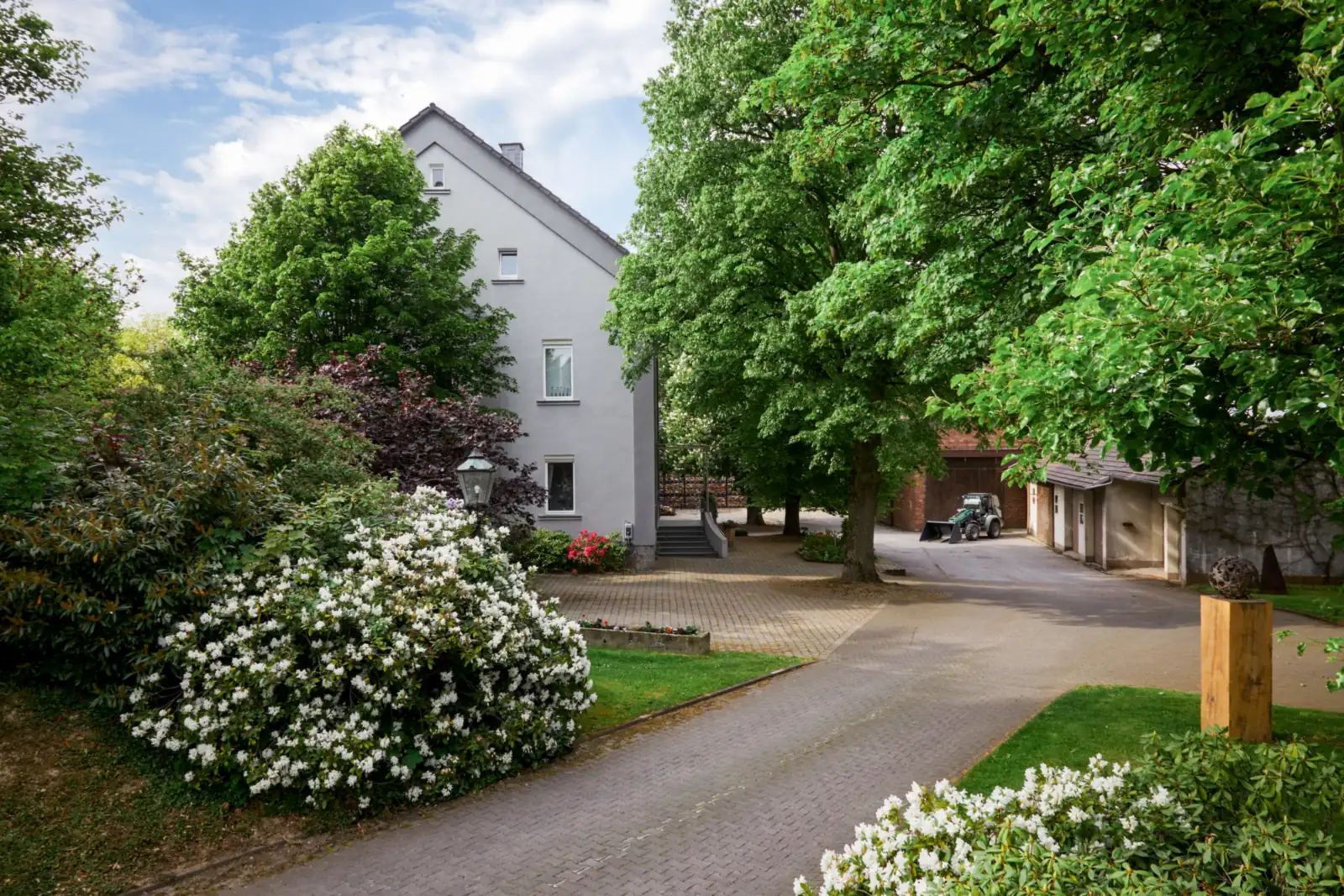 Hofeinfahrt des Hof Schulte mit Wohnhaus, Kastanien und blühenden Sträuchern